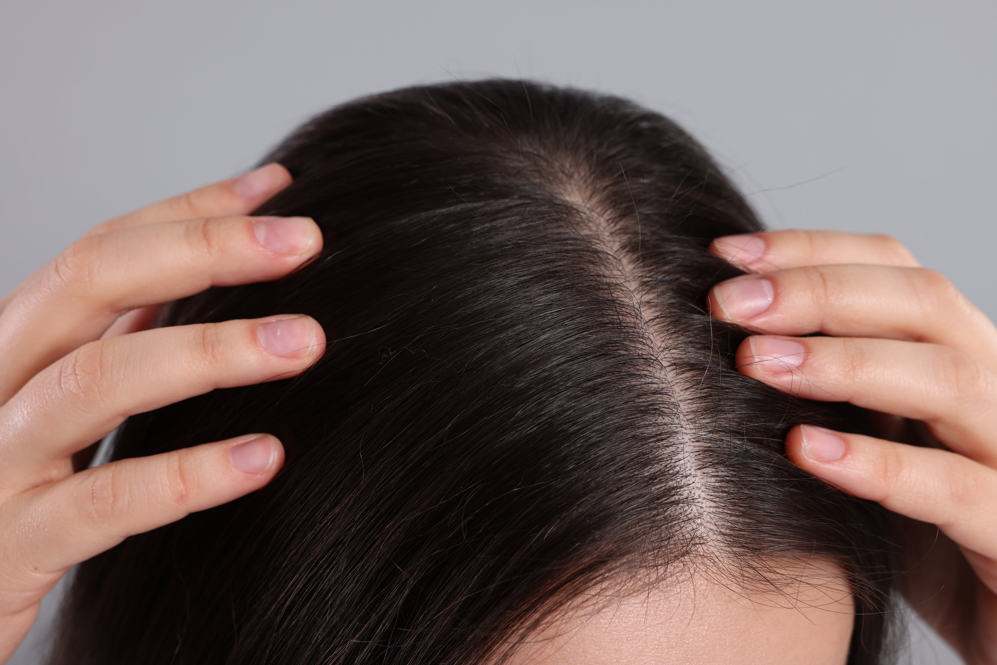 Woman Examining Her Hair and Scalp on Grey Background, Closeup